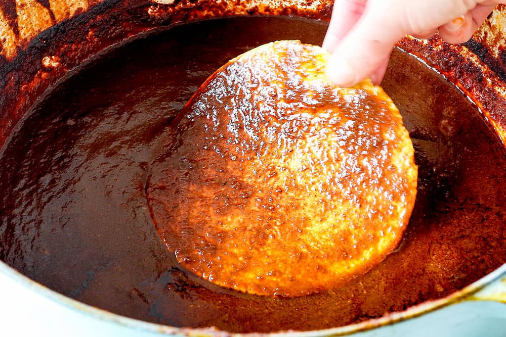showing how to make birria tacos by dipping a corn tortilla in the birria consommé