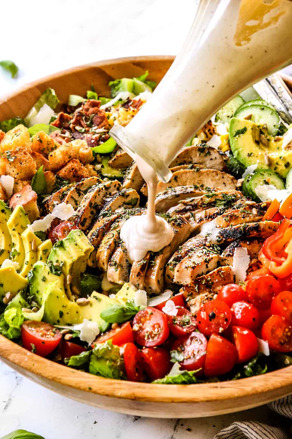 pouring Caesar Dressing over a salad with chicken