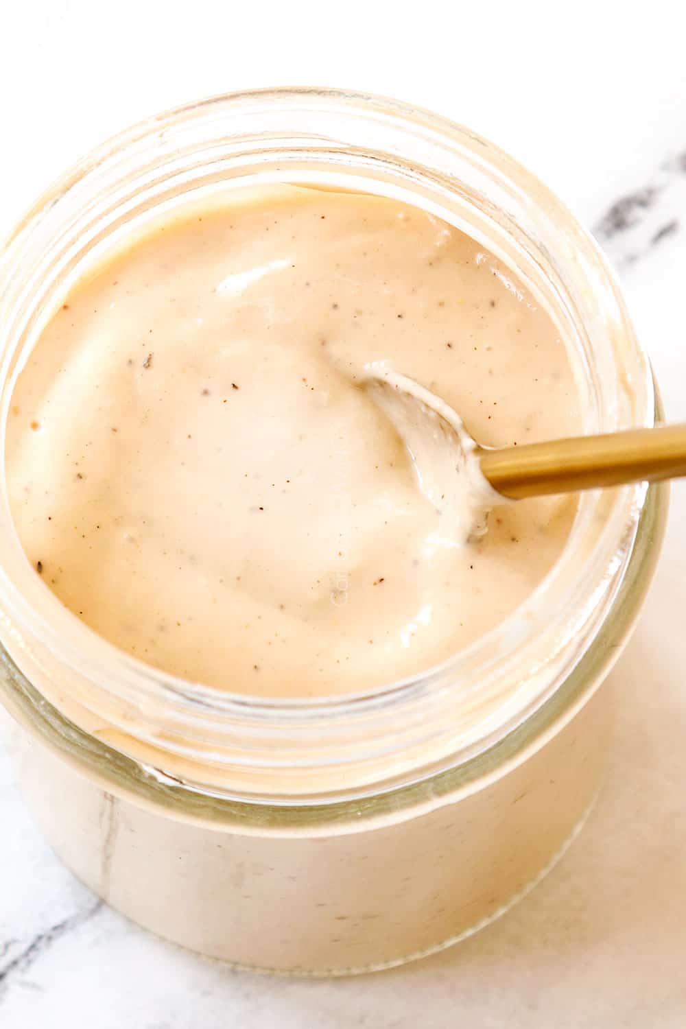 up close of a spoon in a jar of homemade Caesar dressing showing how creamy it is