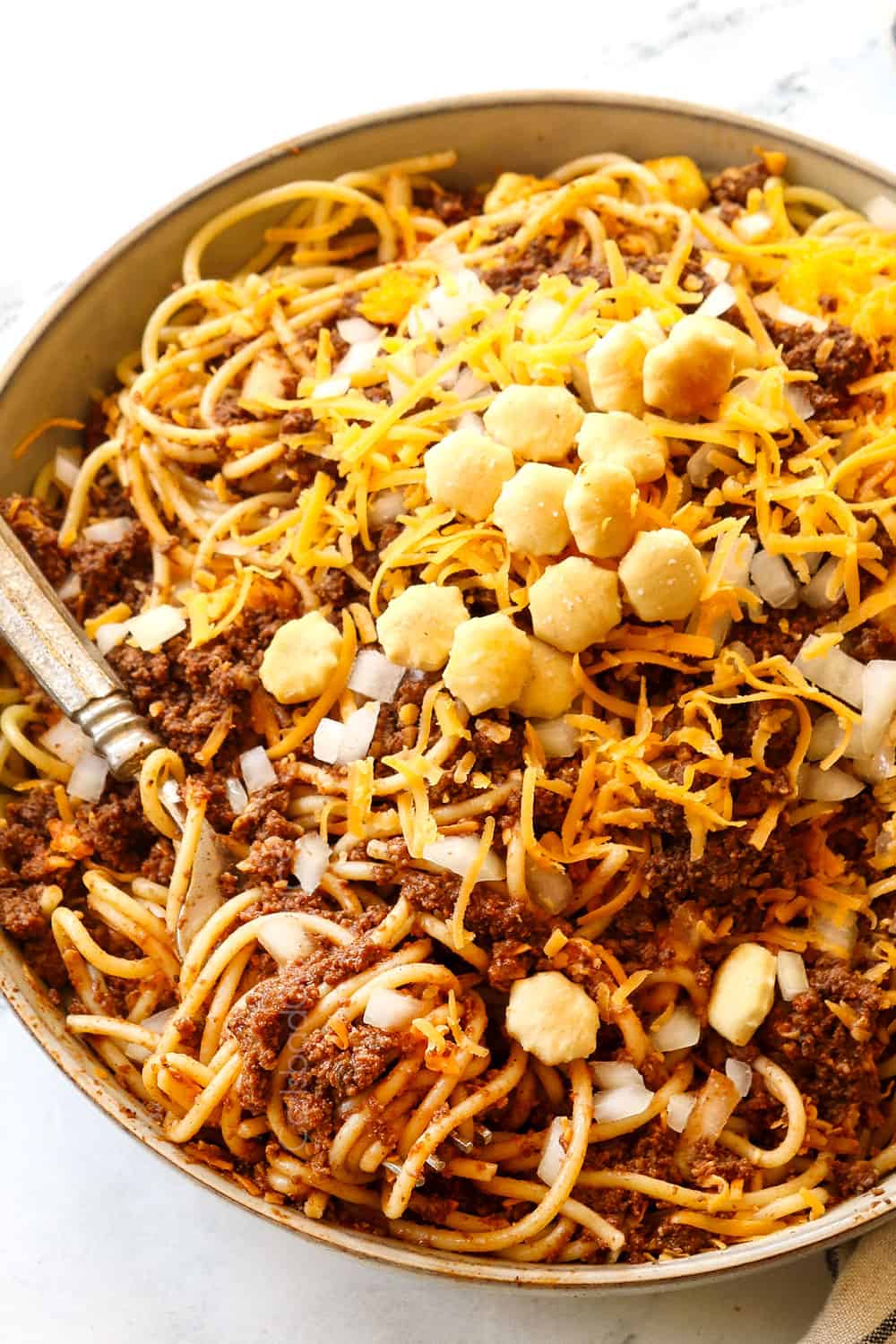 a fork digging into a bowl of Cincinnati chili showing how to eat it