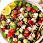 top view of showing how to make Greek Salad recipe by mixing tomatoes, cucumbers, Kalamata olives, red onions and feta together