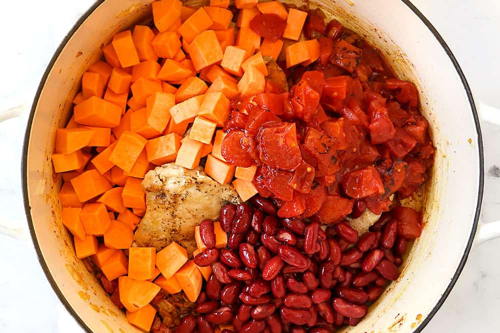 showing how to make African Peanut Stew by adding tomatoes, sweet potatoes and beans to the soup pot
