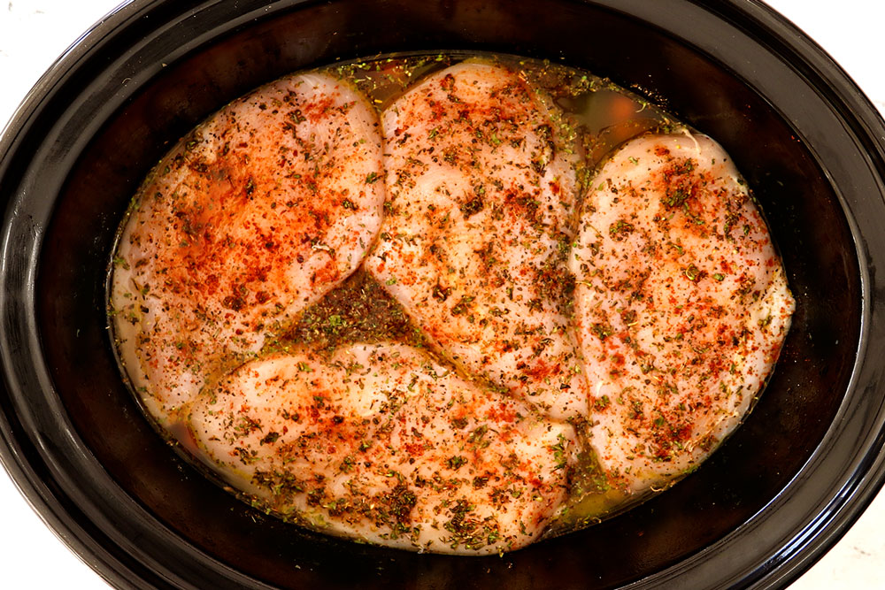 showing how to make Chicken and Rice Crockpot recipe by adding chicken breasts on top of the rice in the slow cooker