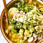 top up close view of showing how to top pozole verde de pollo with radishes, cilantro, avocados and radishes