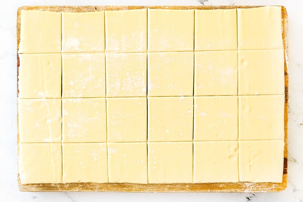 showing how to make cranberry brie bites by rolling out puff pastry and slicing it into 24 squares