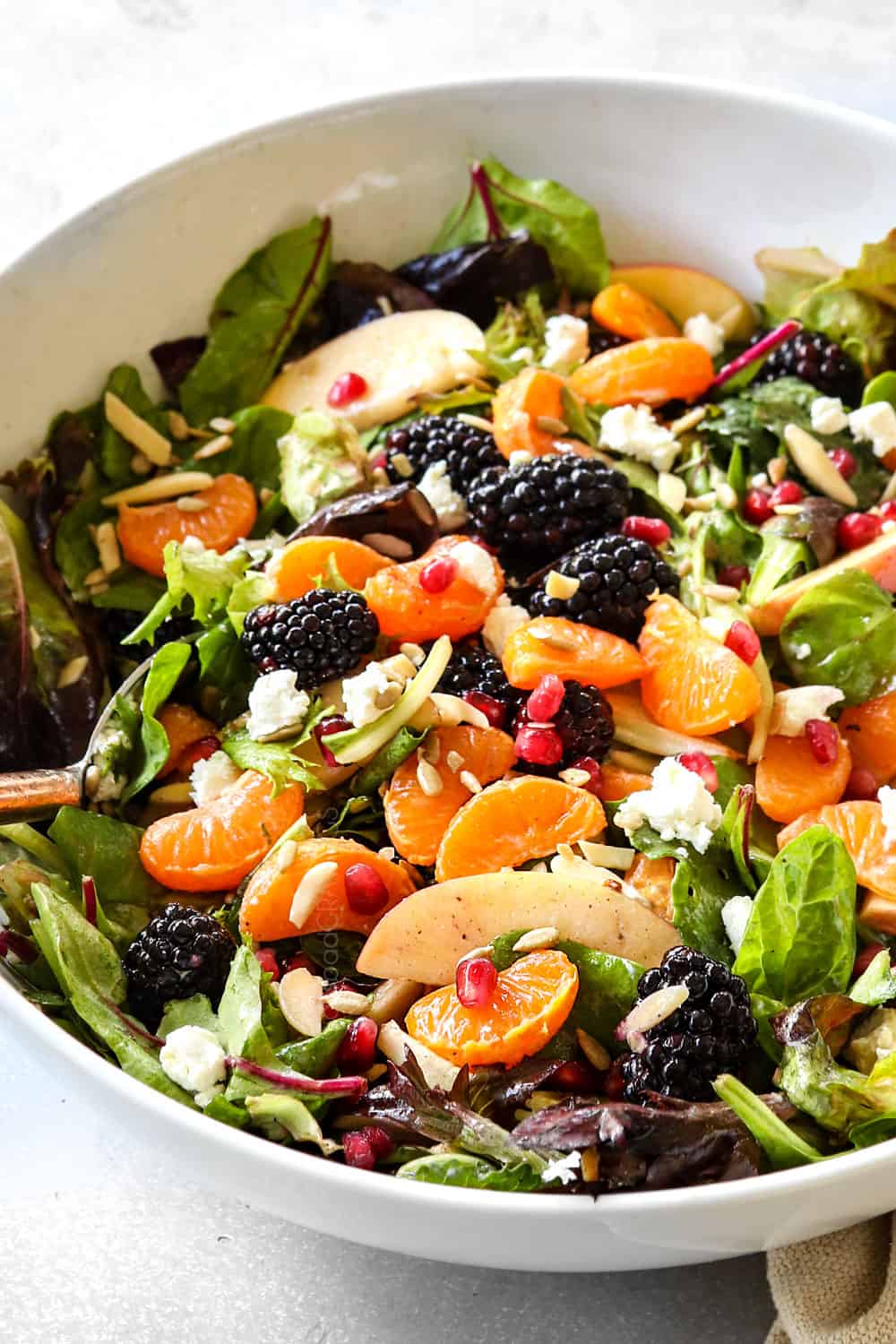 side view tossing mandarin orange salad together with mandarins and goat cheese
