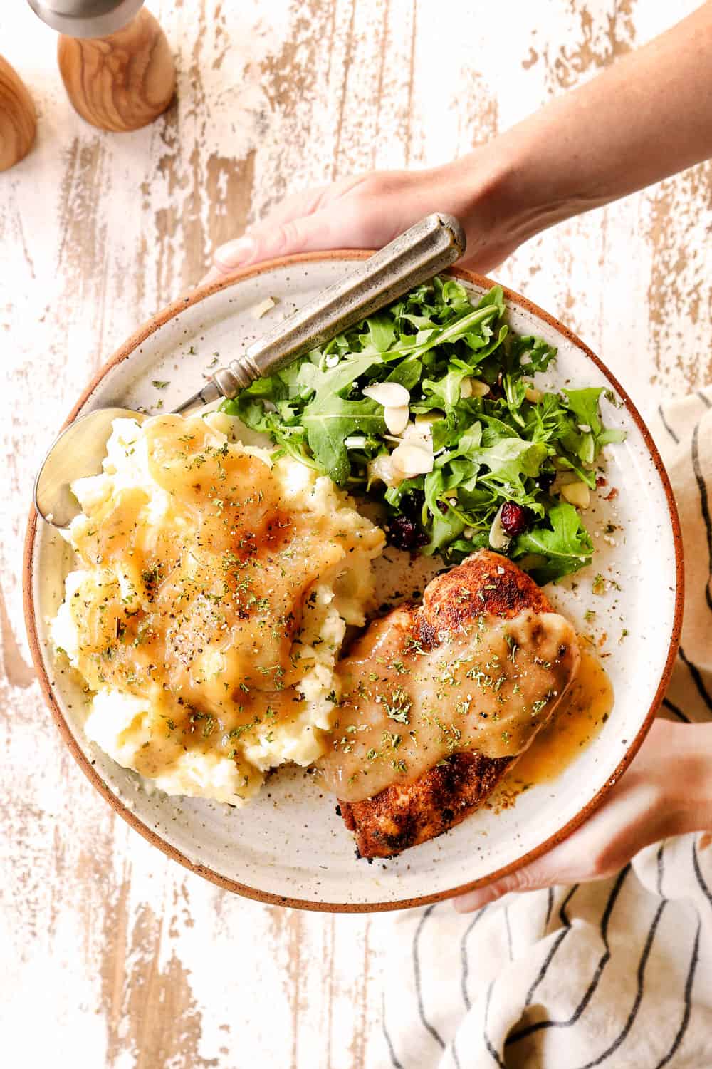 two hands holding a plate with chicken gravy recipes over potatoes