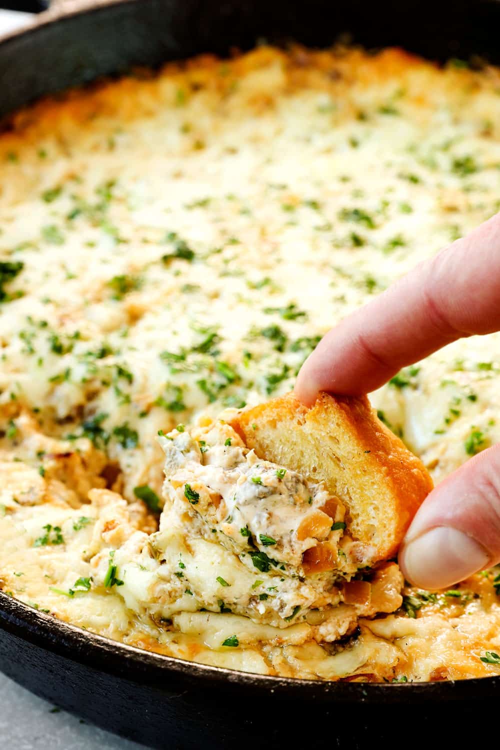 showing how to serve Philly cheesesteak dip by dipping in a baguette slice into the hot dip recipe