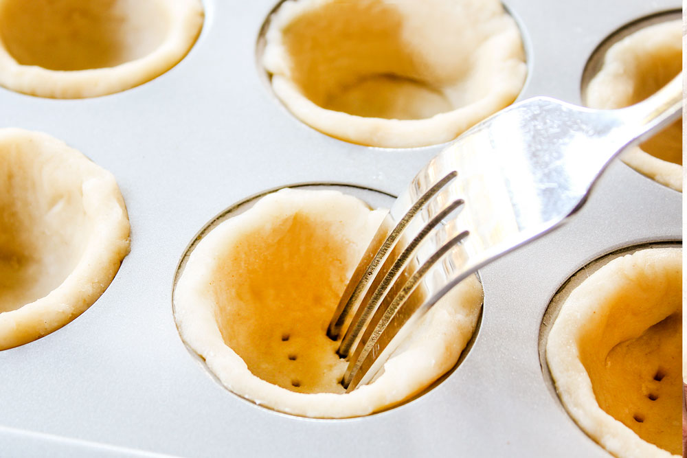 showing how to make mini quiche by adding pastry rounds to the mini muffin tins then docking by pricking with a fork