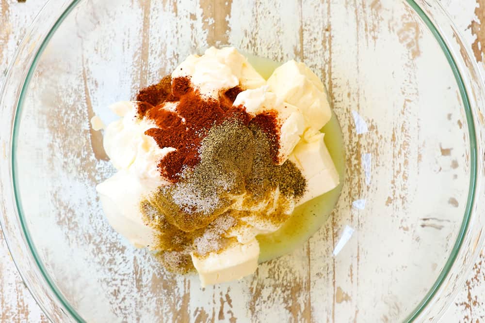 showing how to make Mexican corn dip recipe by adding cream cheese, sour cream and mayonnaise, chili powder, ground cumin and onion powder to a glass bowl