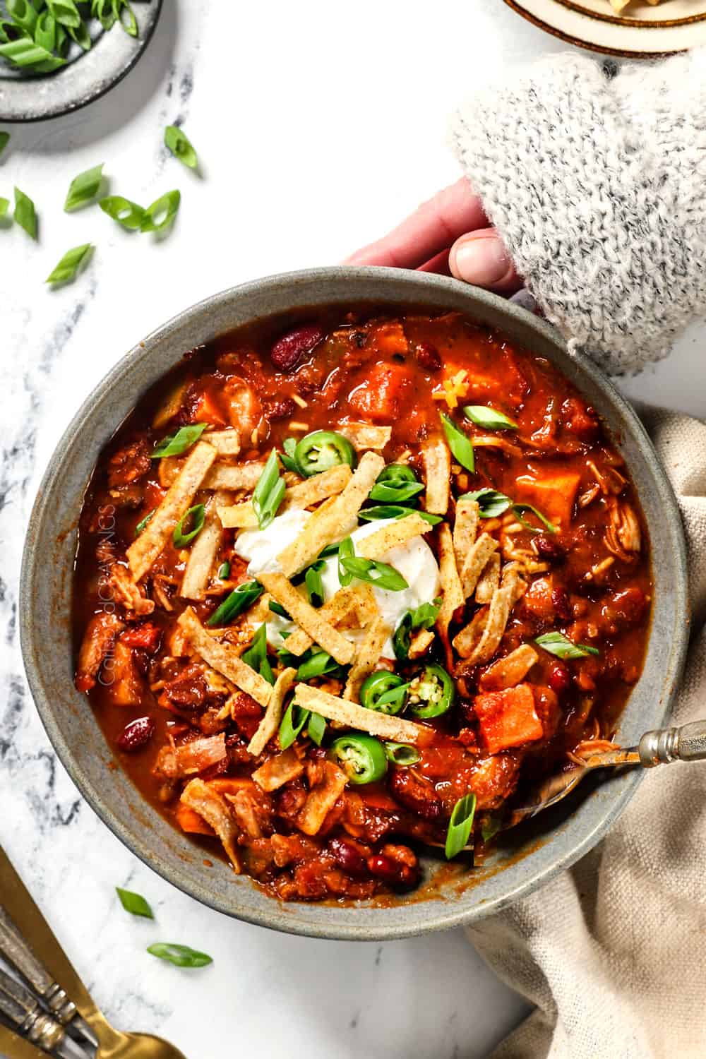 top view of two hands holding a bowl of healthy chicken chili with sweet potatoes