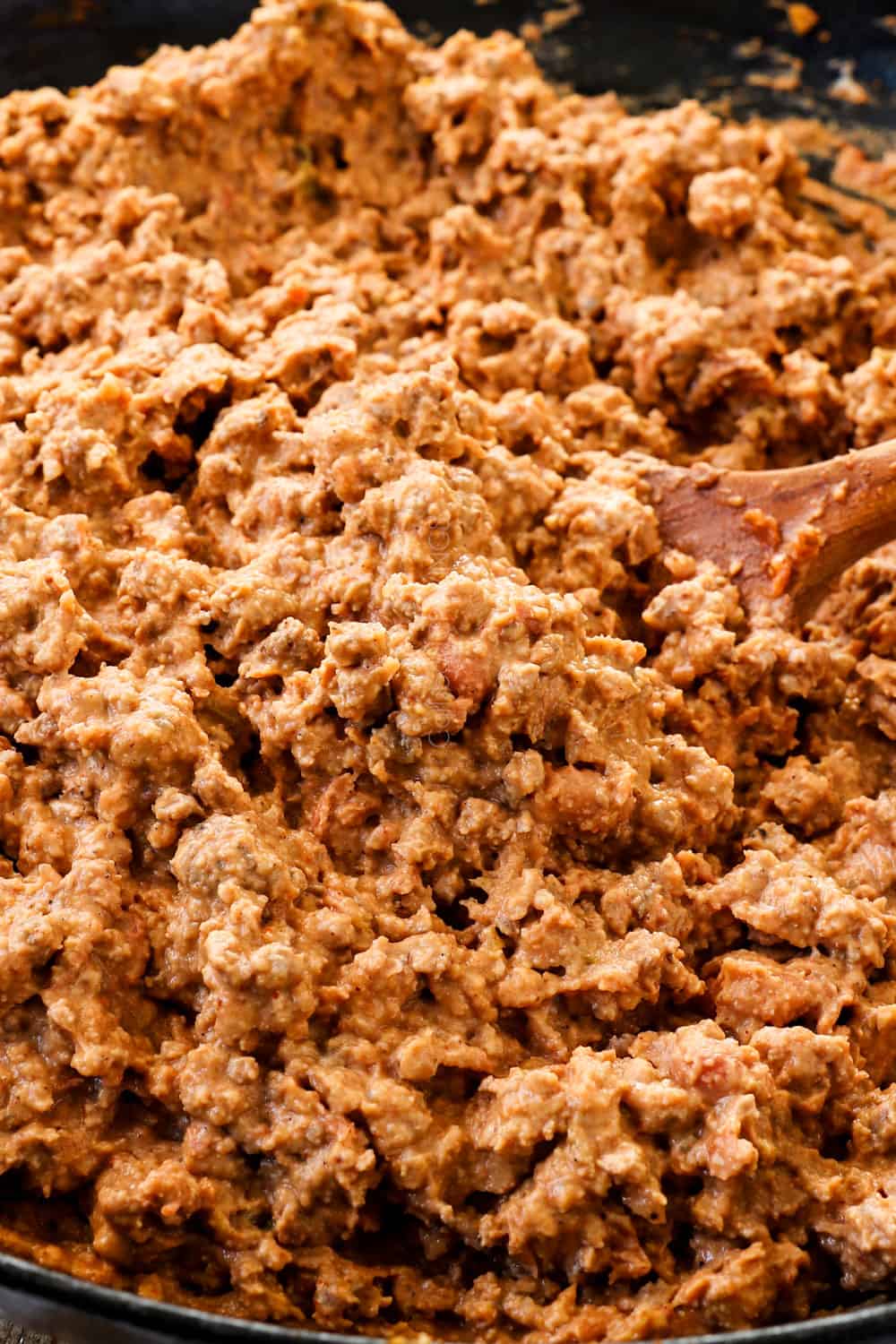 showing how to make nacho recipe by stirring refried beans together with ground beef in a skillet