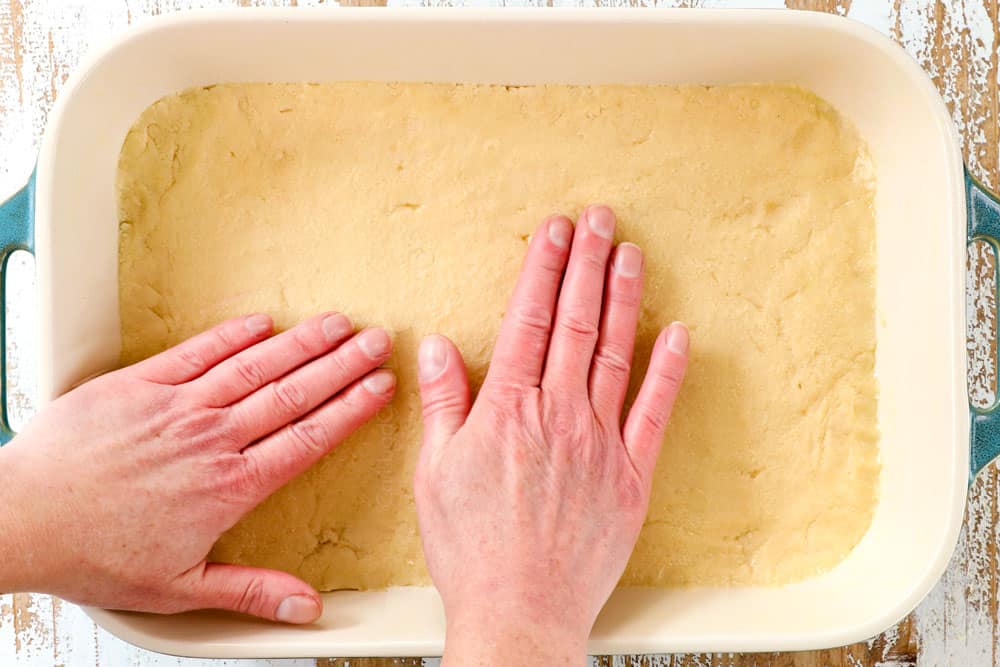 showing how to make Ooey Gooey Butter Cake recipe by pressing the cake layer into the bottom of a 9x13 pan