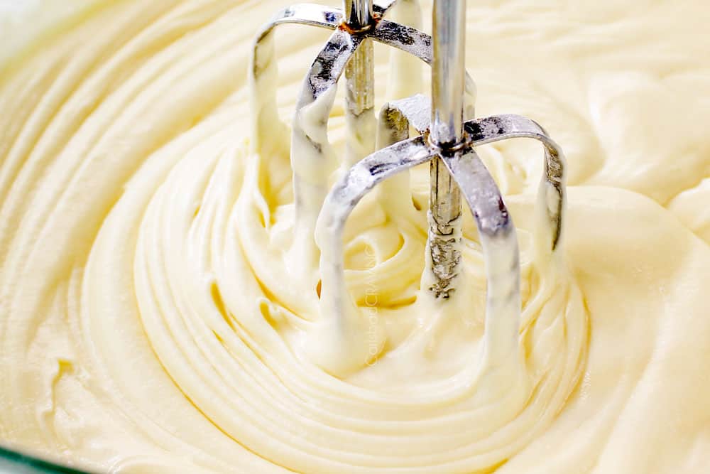 showing how to make Ooey Gooey Butter Cake recipe by adding powdered sugar to cream cheese layer and beating until smooth with a hand held mixer