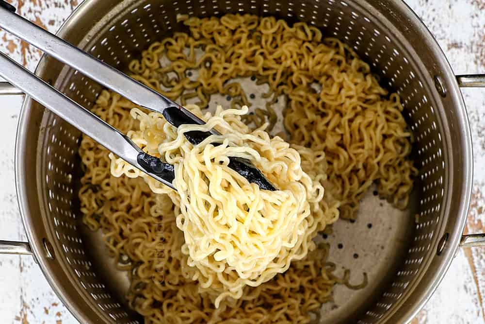 showing how to make ramen noodles recipe by cooking and straining ramen noodles and tossing with sesame oil