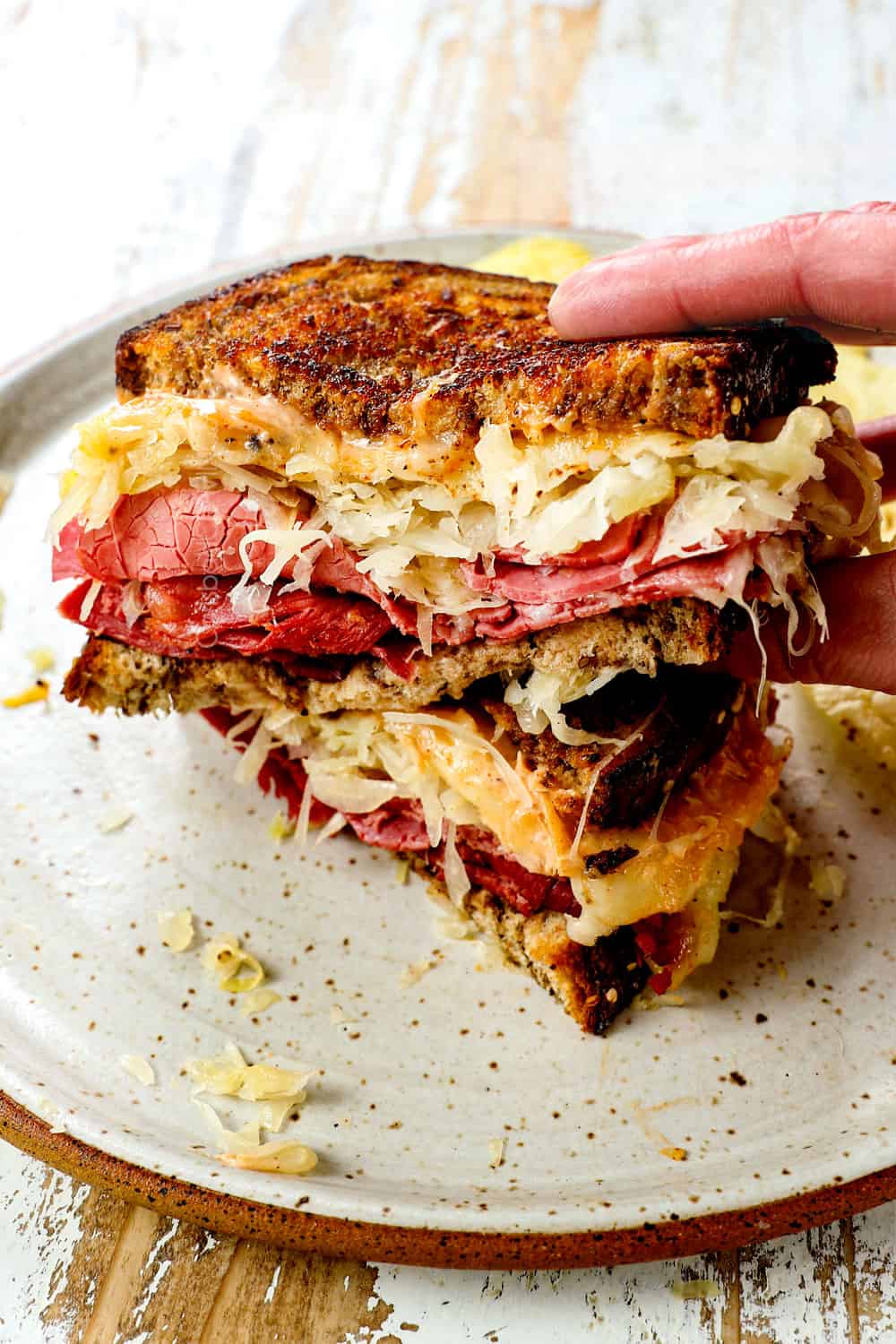 a hand picking up a Reuben Sandwich with grilled rye bread, sliced corned beef sauerkraut, Swiss cheese and Russian dressing