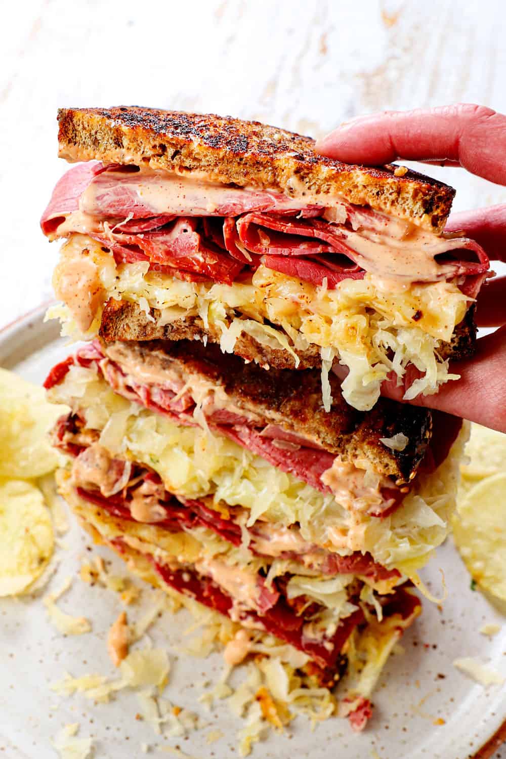 a stack of Reuben sandwiches sliced in half with a hand picking up one sandwich