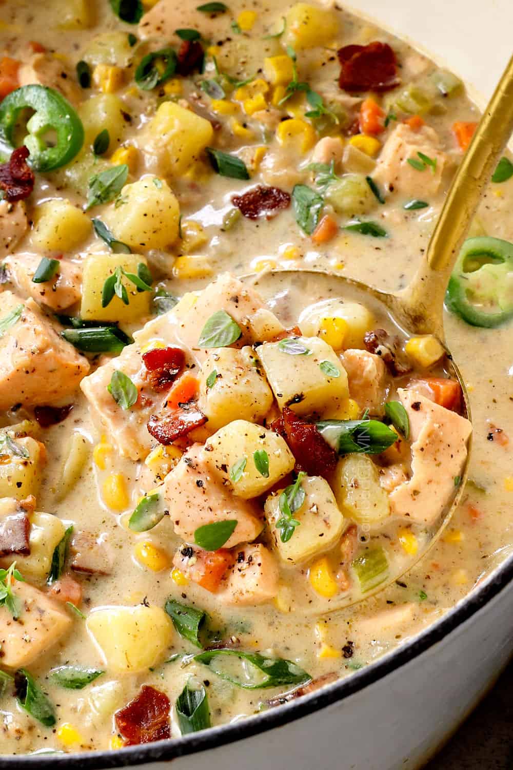up close of a ladle of salmon chowder (fish chowder) with salmon, potatoes, carrots, celery and bacon showing how rich, hearty and creamy it is