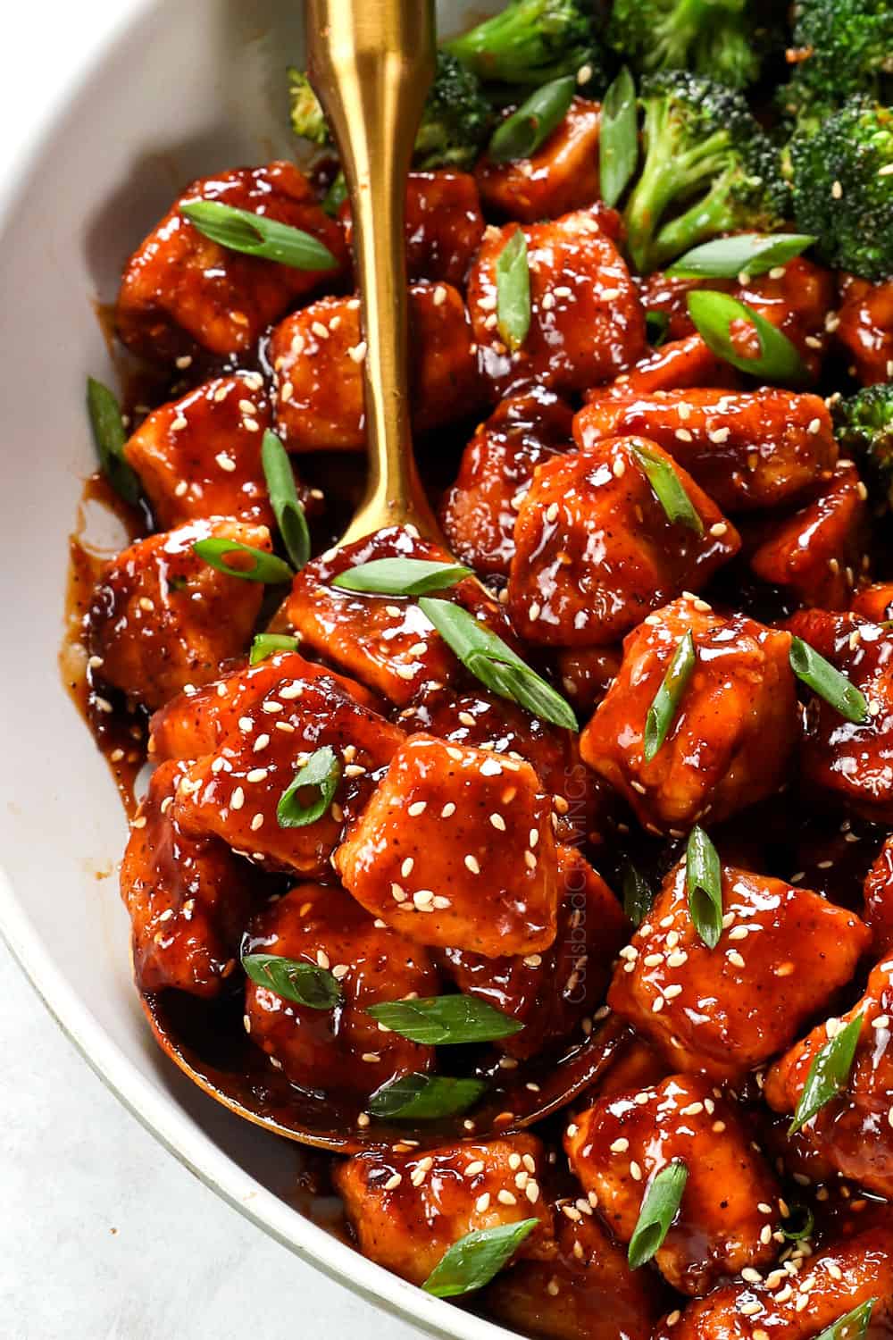 up close of a spoonful of honey sesame chicken garnished with toasted sesame seeds