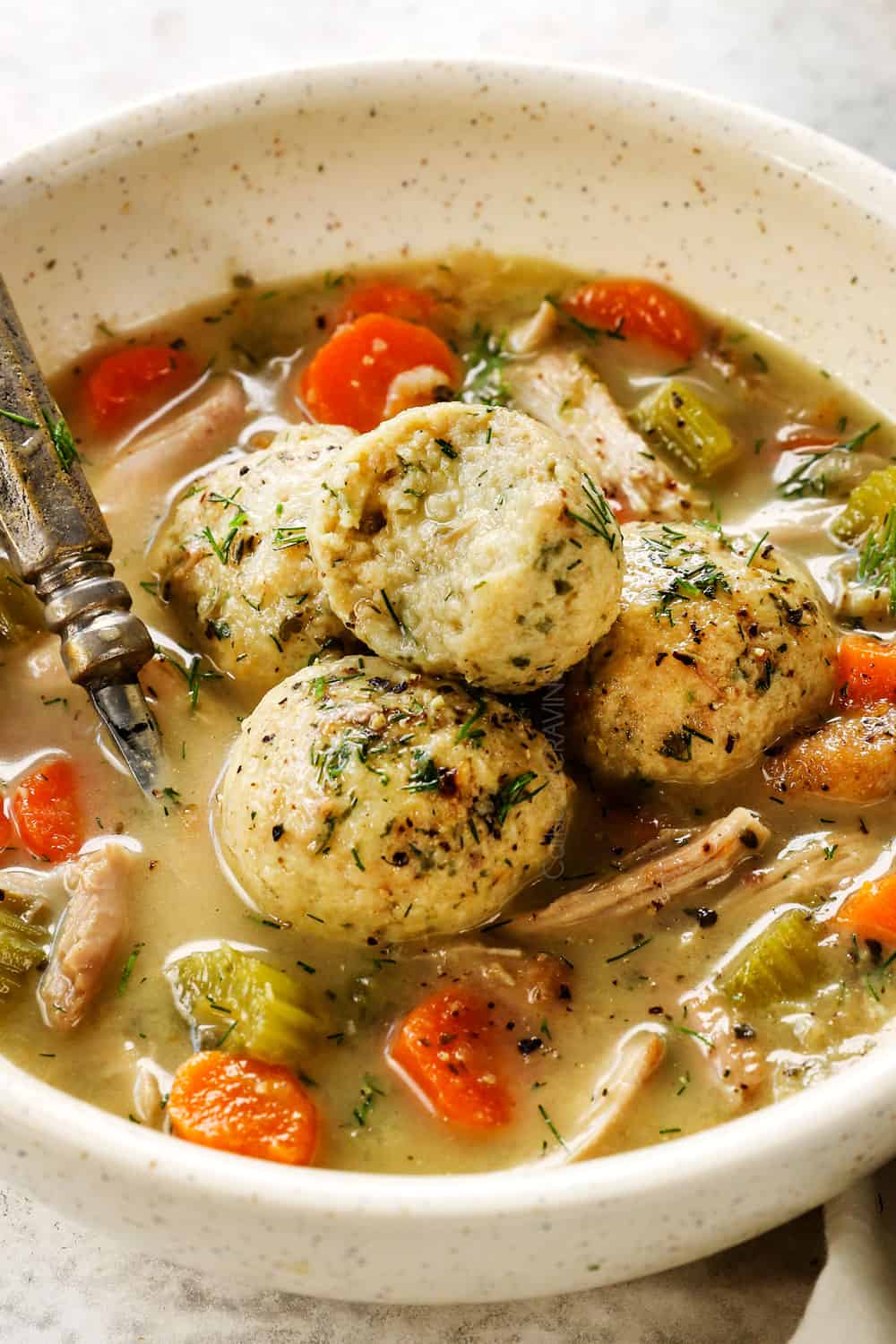 up close of a bowl of matzo ball soup recipe with a bite taken out of a matzo ball showing how soft and fluffy it is