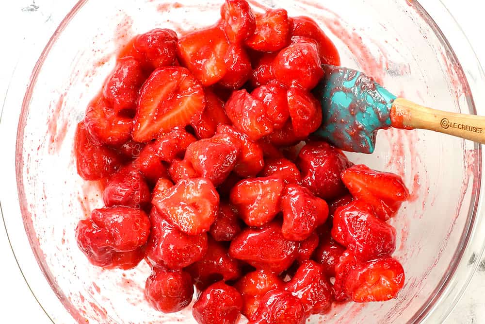 showing how to make strawberry topping for cheesecake by stirring strawberries into glaze