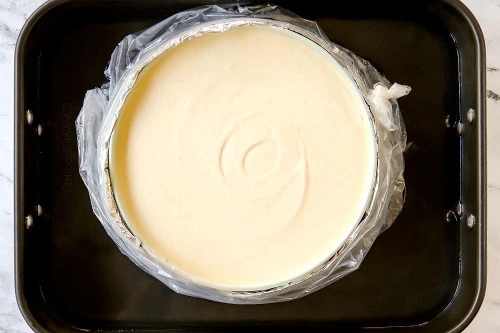 showing how to bake a cheesecake in a water bath by placing foil lined springform pan in a roasting pan with hot water