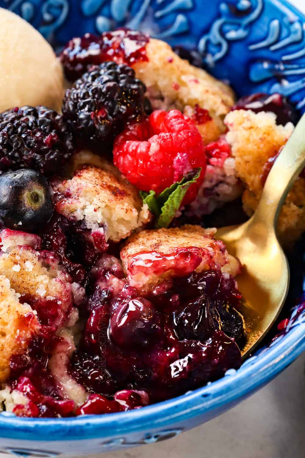 up close of a spoonful of with blackberries, blueberries, raspberries and strawberries mixed berry cobbler