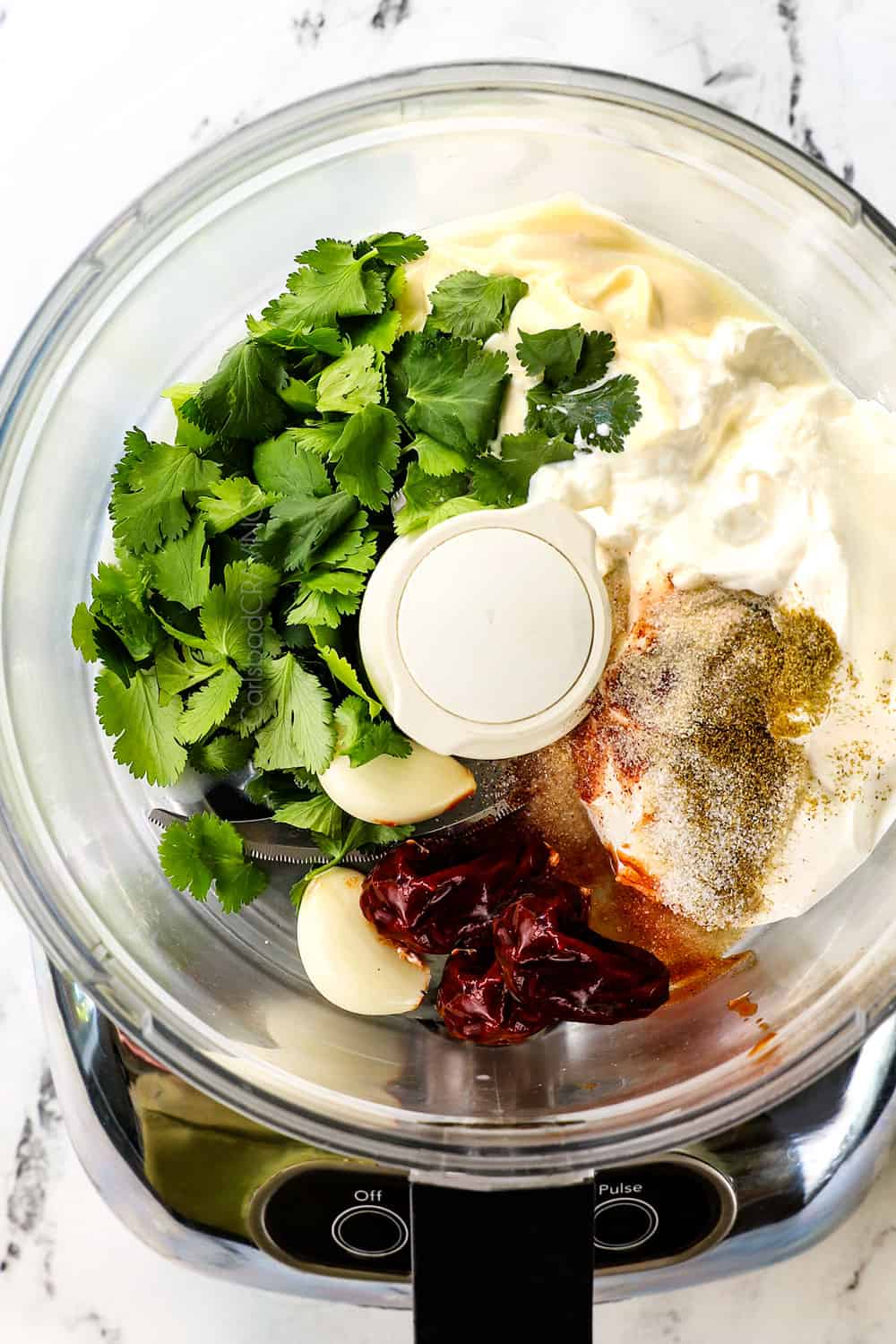 showing how to make chipotle sauce recipe by adding chipotle peppers in adobo, adobo sauce, sour cream, mayonnaise, garlic, lime juice and cilantro to a food processor