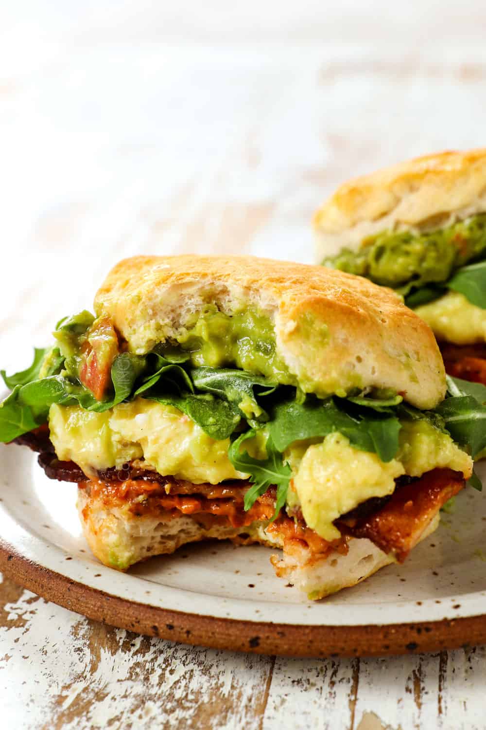 breakfast sandwiches with a bite taken out showing the cheesy eggs, and bacon