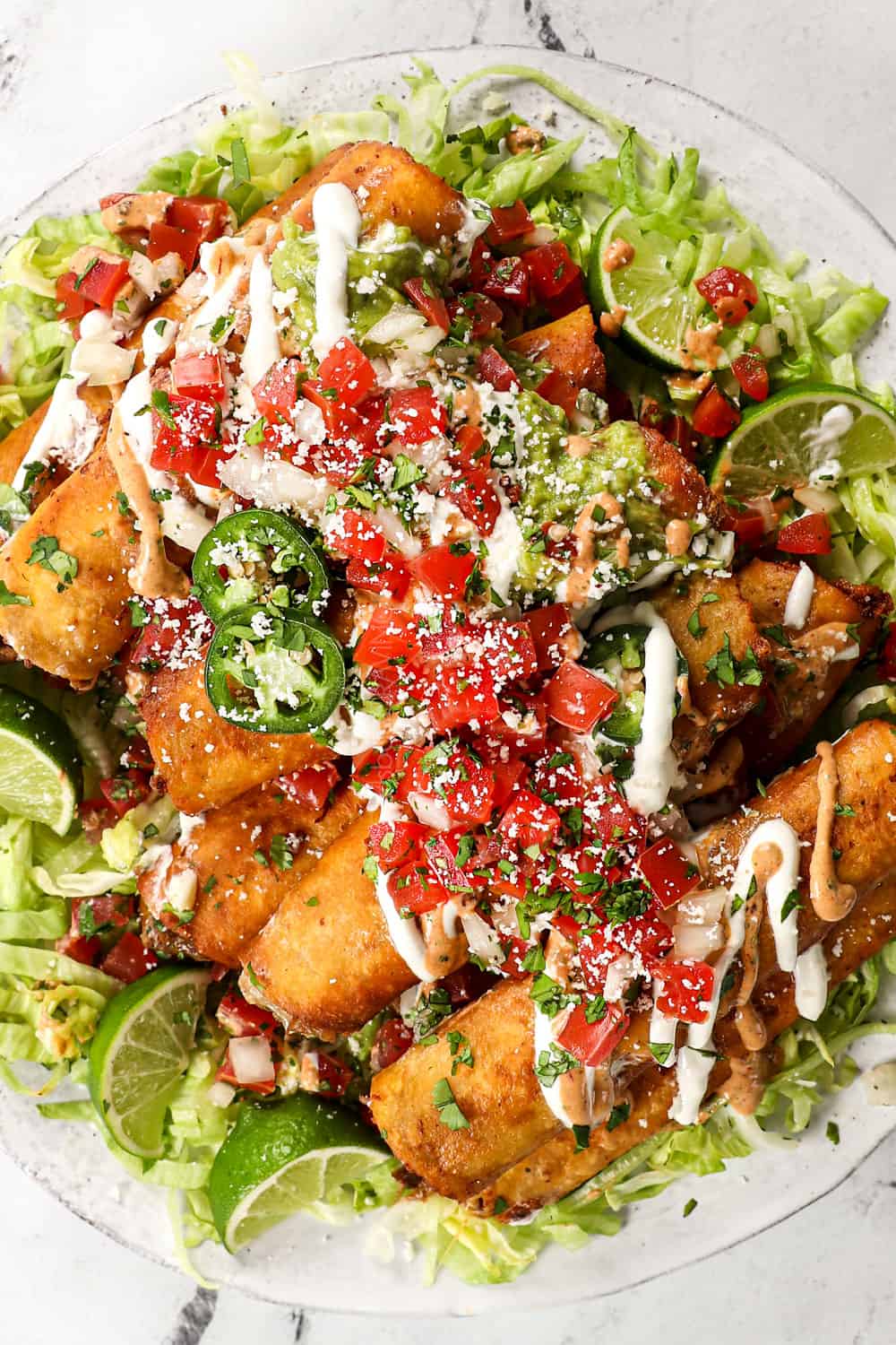 top view showing how to serve taquitos with shredded lettuce, guacamole, sour cream, pico de gallo and jalapenos