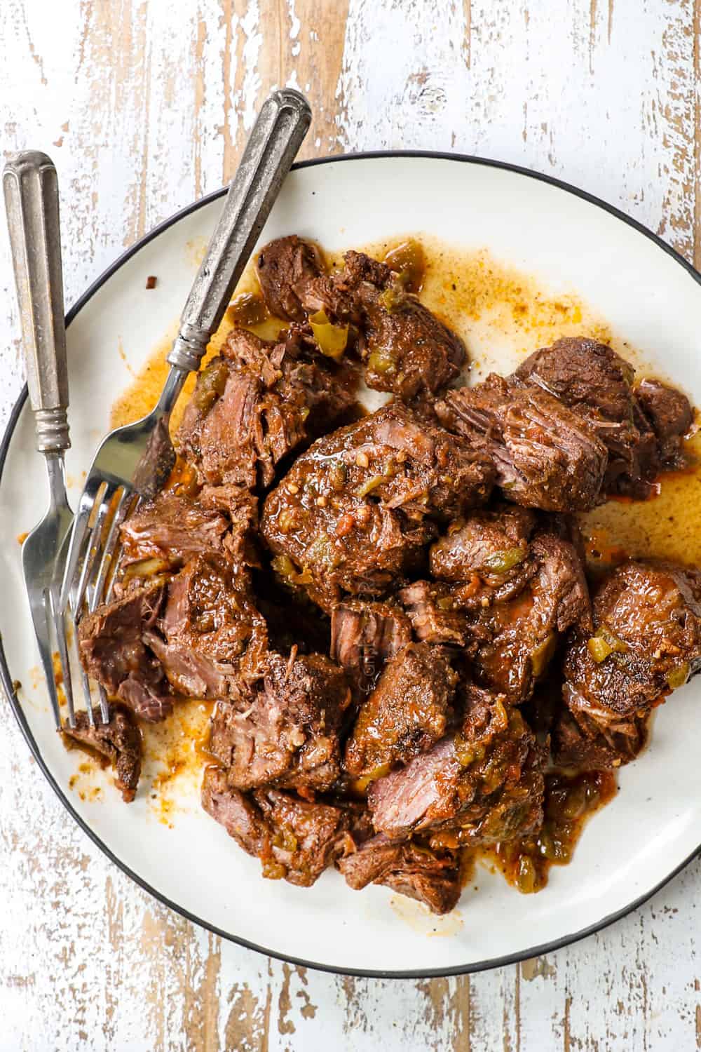 showing how to make taquitos by shredding beef on a plate with two forks