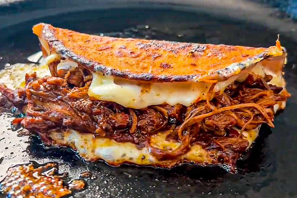 showing how to make chicken birria tacos recipe by cooking chicken and cheese in the taco in a skillet