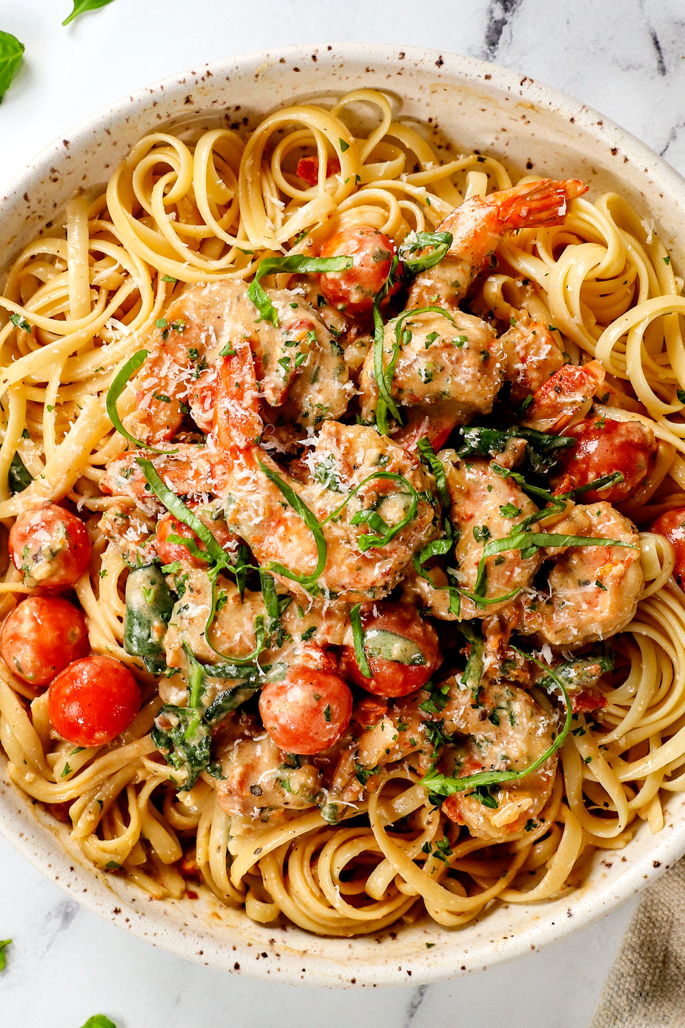 showing how to serve garlic Tuscan shrimp by serving over pasta in a bowl with freshly grated Parmesan