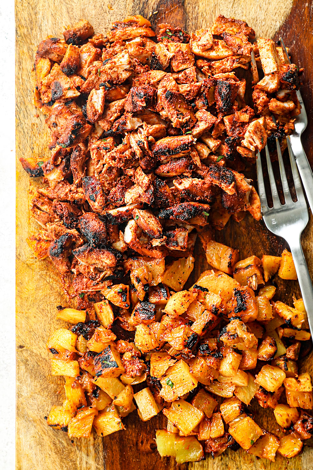 showing how to make al pastor chicken by carving chicken and pineapple on a cutting board into small pieces