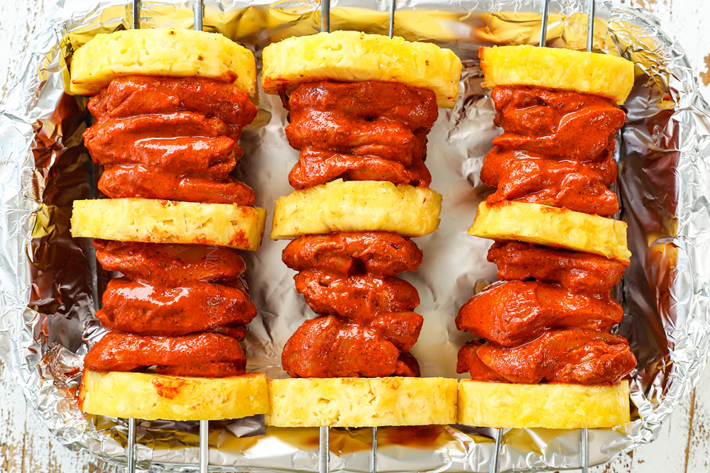 showing how to bake chicken al pastor by lining the skewers over a baking pan so they aren't touching the bottom