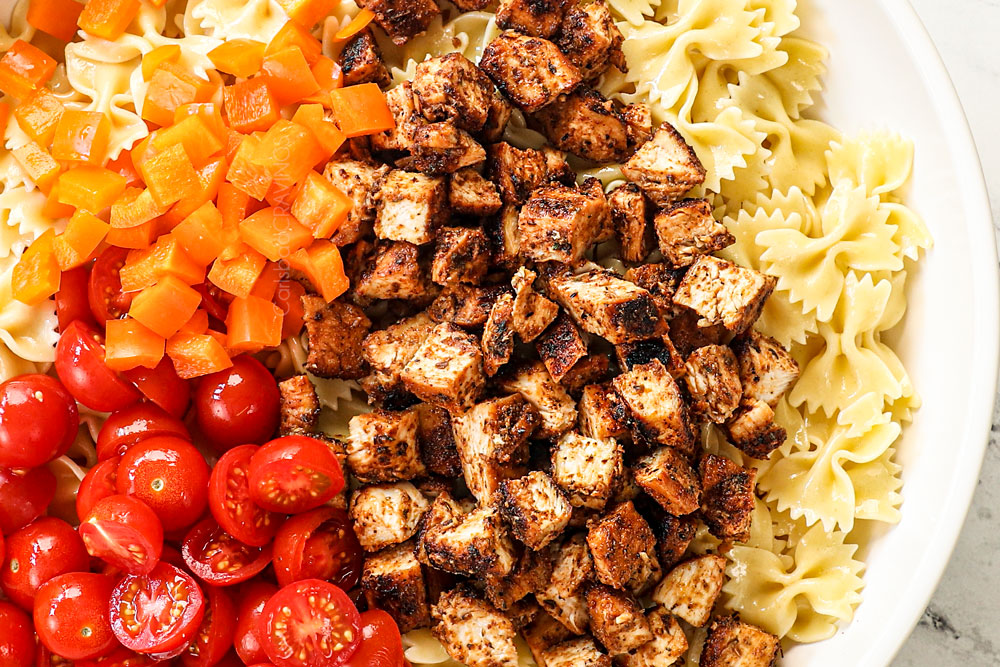 showing how to make Caesar Pasta Salad by adding pasta, chicken and tomatoes to a large bowl