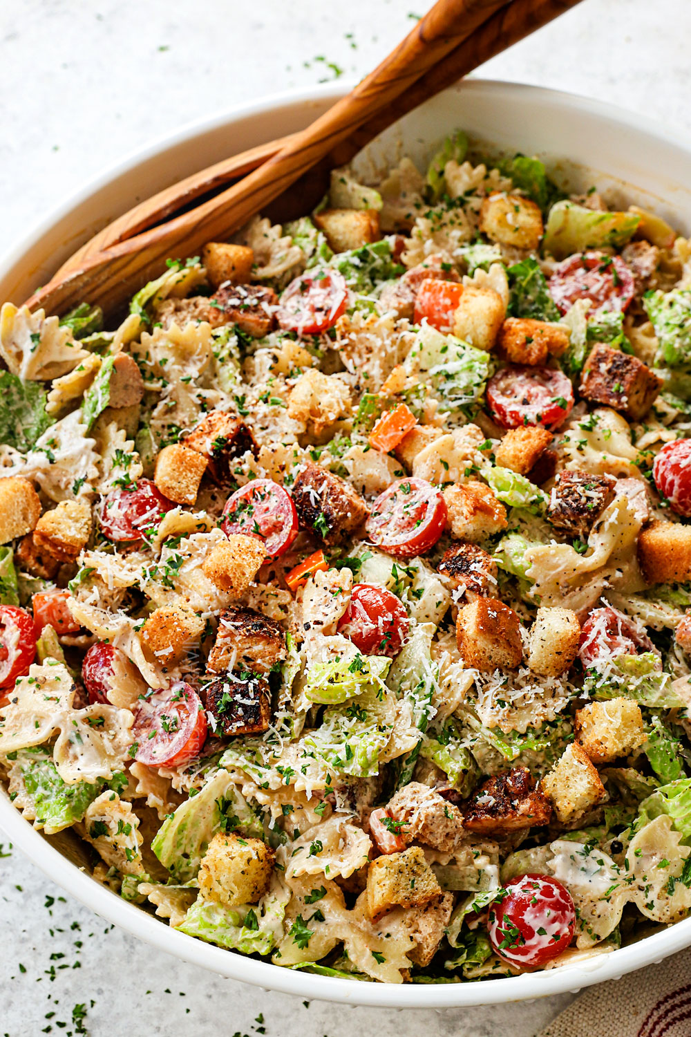 up close of serving Chicken Caesar Pasta Salad in a white bowl with freshly grated Parmesan cheese