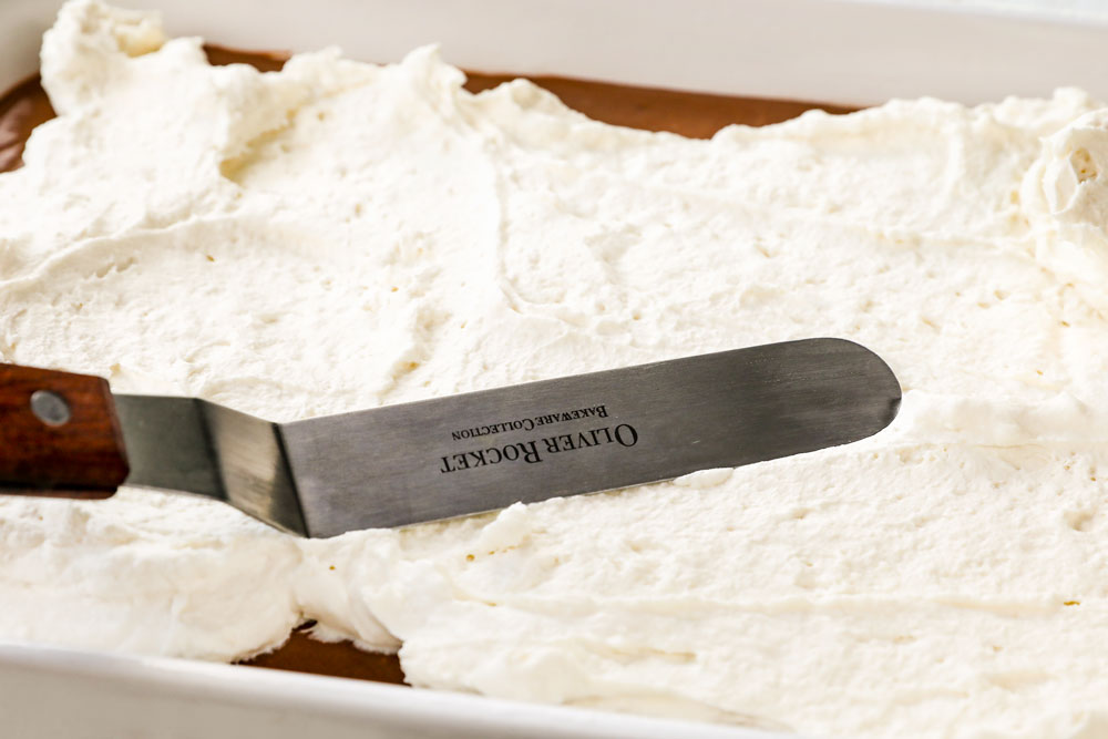 showing how to make chocolate lasagna recipe by spreading homemade whipped topping over the chocolate pudding layer