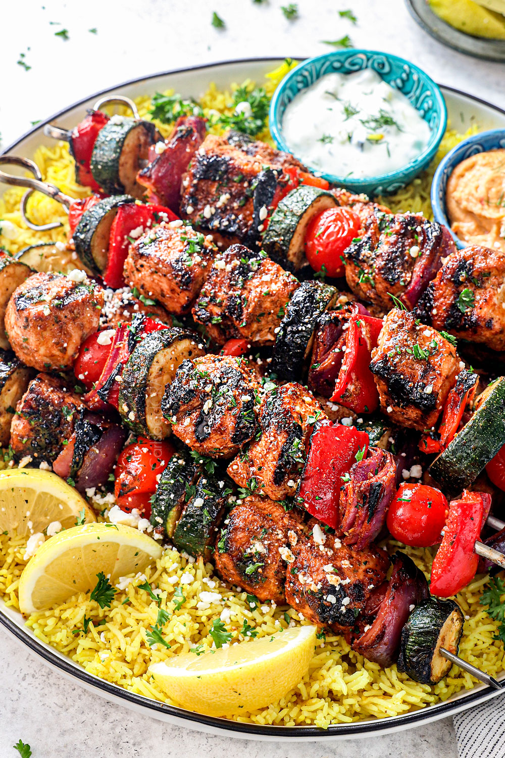 side view of Greek Chicken kabobs stacked on a platter garnished with feta and parsley showing how to serve