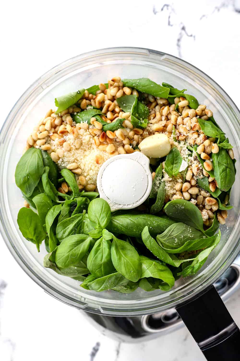 top view showing pesto ingredients in a food processor: basil, pine nuts, Parmesan and garlic