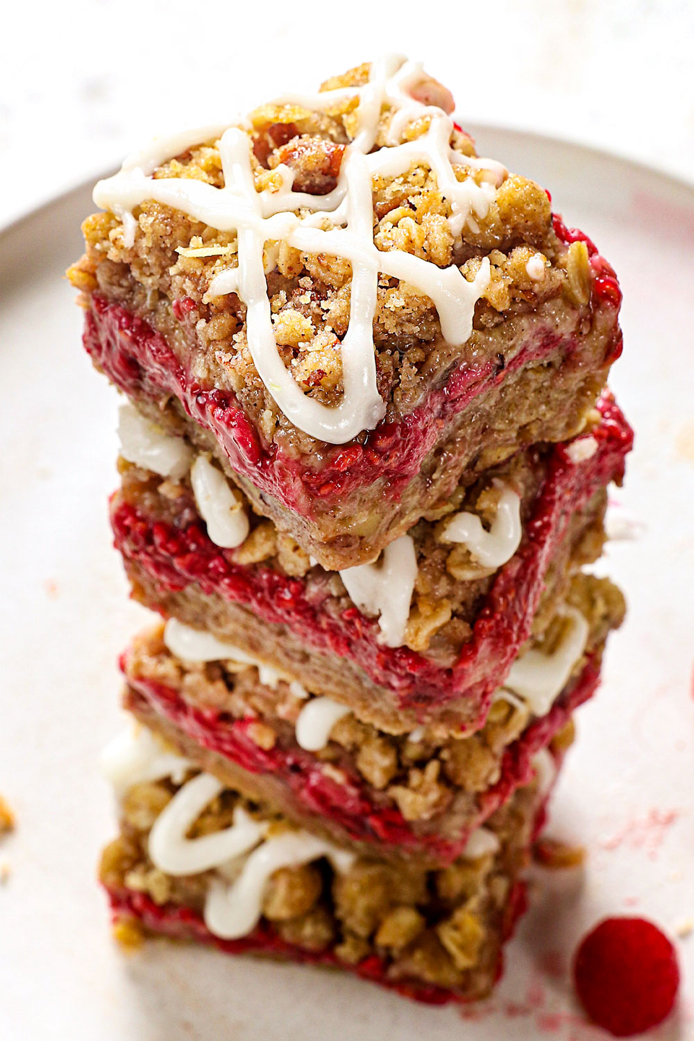 a stack of raspberry bars with crumble topping with lemon icing drizzle showing how crunchy the topping is