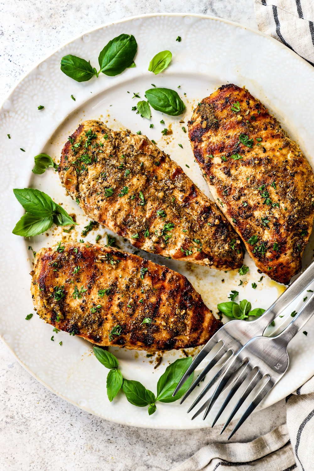 three chicken breasts marinated in Italian Chicken Marinade garnished with basil on a white plate