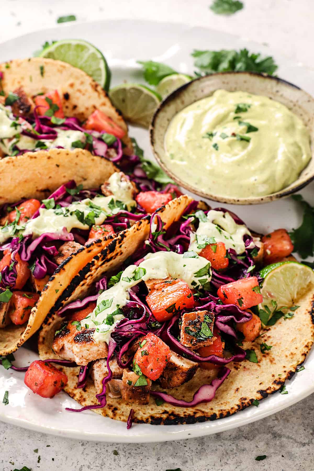 jerk chicken tacos being served on a plate with pineapple slaw and avocado crema