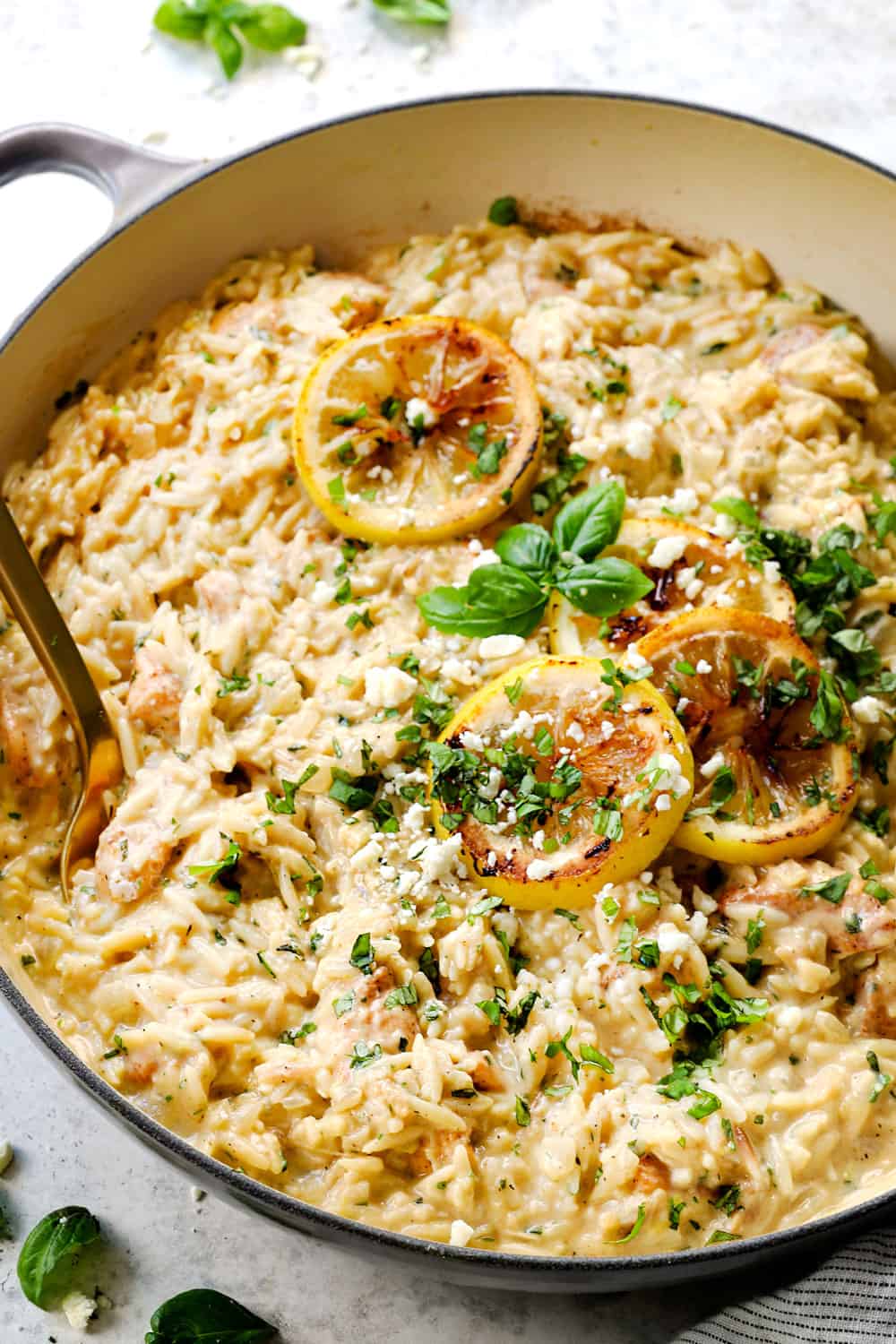 lemon orzo with chicken in a skillet garnished by lemon slices, basil and feta