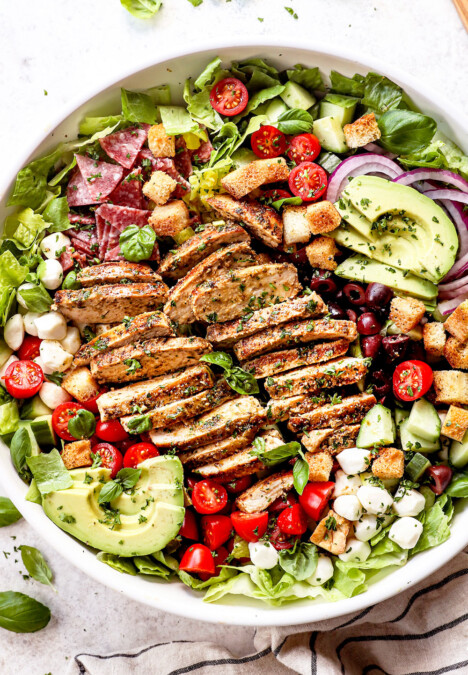 top view showing how to make Mediterranean Chicken Salad by assembling the chicken salad recipe with chicken, tomatoes, cucumbers, olives, red onions and avocado