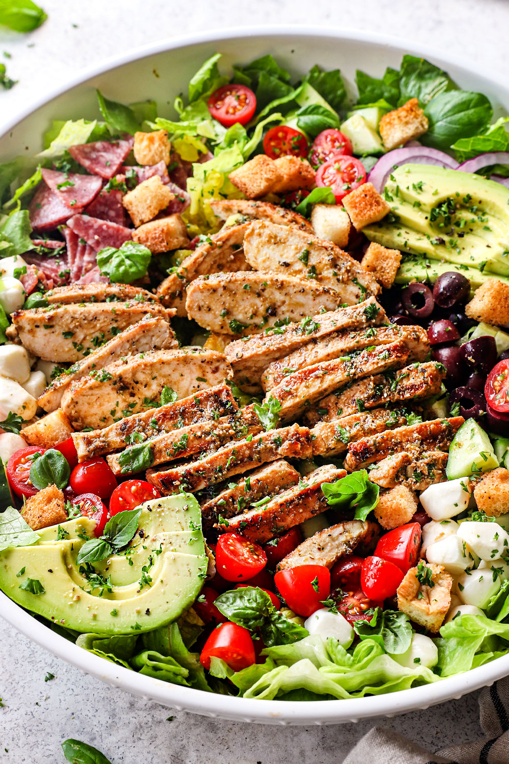 showing how to serve Mediterranean Chicken Salad by adding to a big bowl and garnishing with croutons and parsley