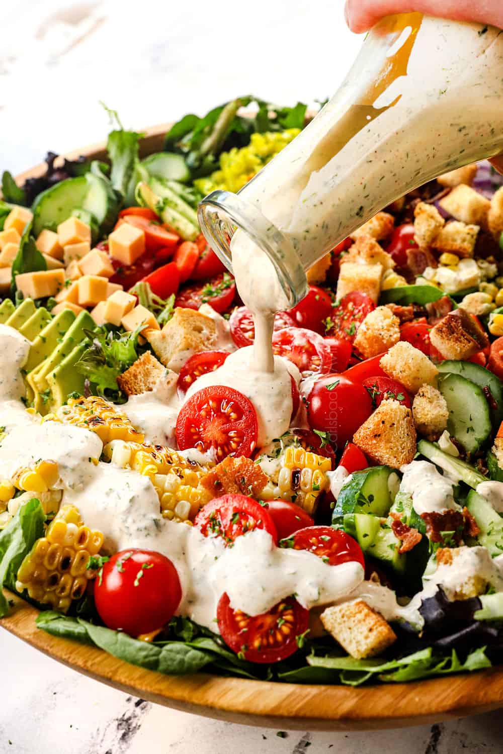 showing how to make garden salad by drizzling the ranch dressing over the salad