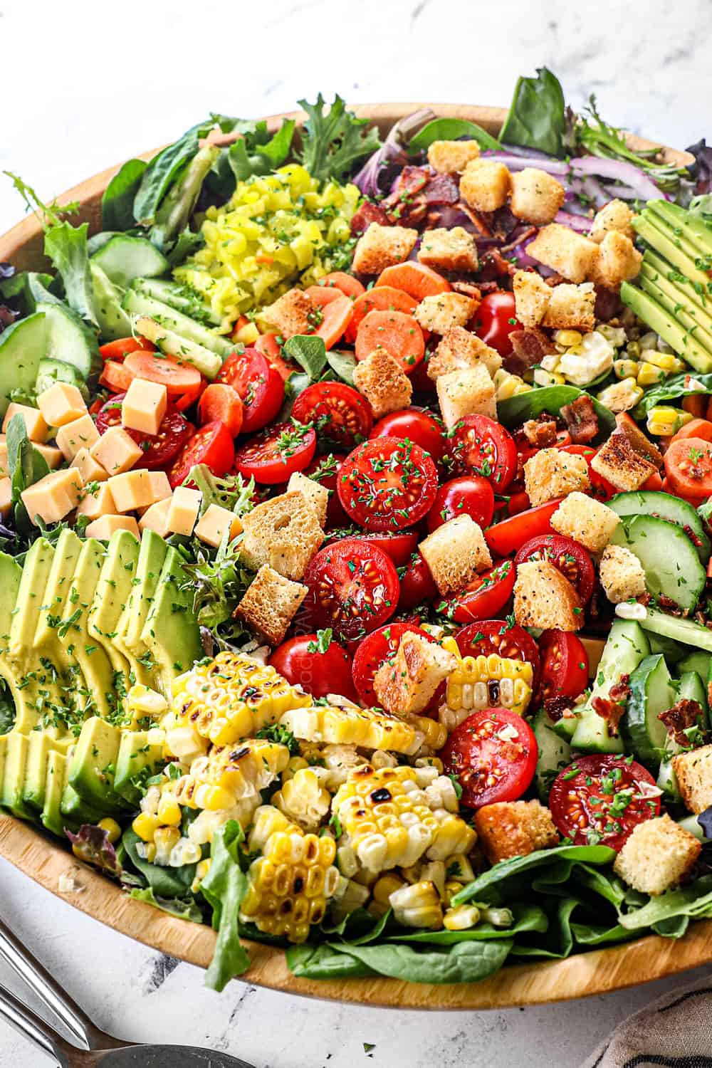 adding garden salad ingredients to a bowl and garnishing with parsley