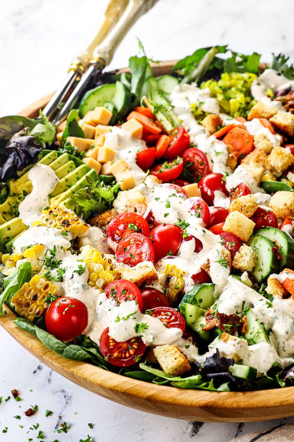garden salad in a bowl with tomatoes, croutons, cheese and bacon drizzled with ranch