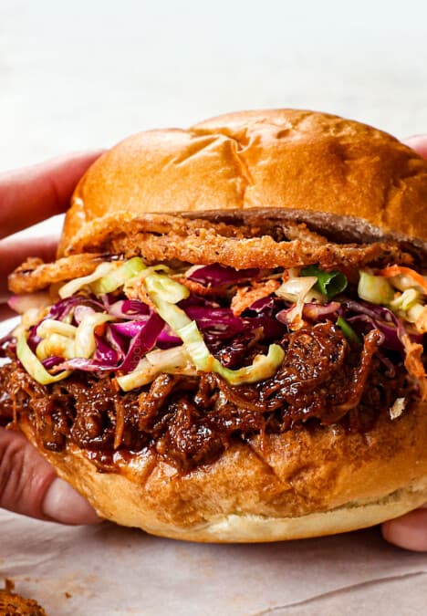 showing how to make BBQ pulled pork sandwiches by topping buns with pulled pork, with coleslaw and fried onion rings